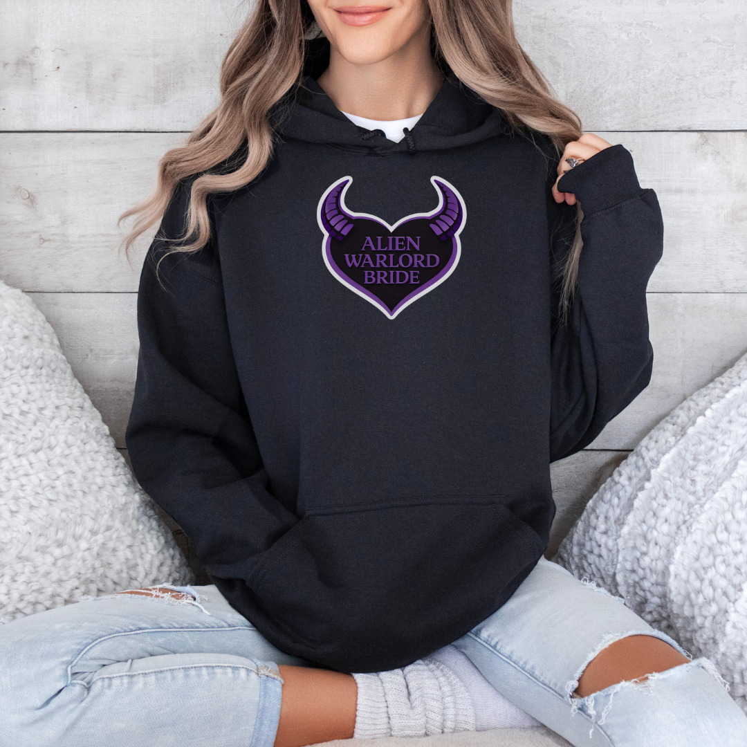 Person wearing a black hoodie with a purple 'Alien Warlord Bride' design, sitting on a textured surface.