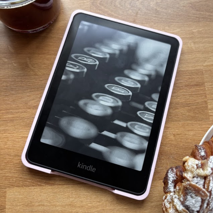 A pink Kindle e-reader displaying a black and white typewriter image on a wooden table.