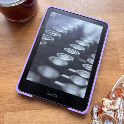 Amazon Kindle e-reader in a purple case on a wooden table with coffee and a pastry