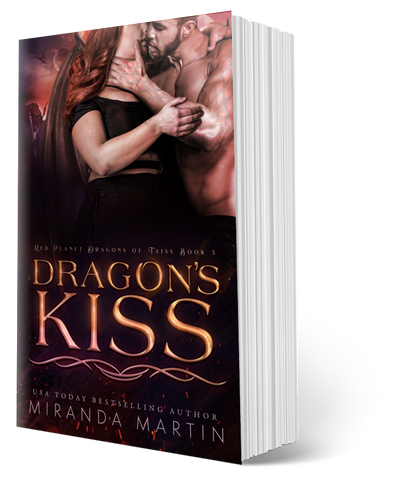 This image displays the paperback version of the book titled "Dragon's Kiss" by Miranda Martin, the fifth book in the Red Planet Dragons of Tajss series. The cover features an intense and romantic scene with the main characters, a human woman and an alien dragon-man, embracing closely in a setting that hints at the book's sci-fi and fantasy elements.
