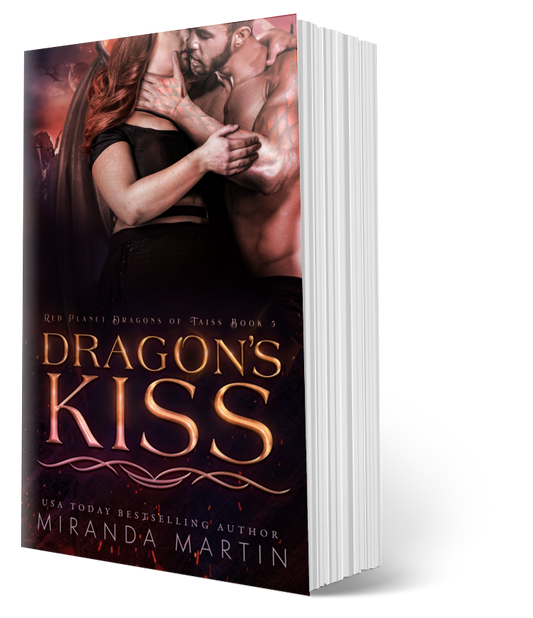 This image displays the paperback version of the book titled "Dragon's Kiss" by Miranda Martin, the fifth book in the Red Planet Dragons of Tajss series. The cover features an intense and romantic scene with the main characters, a human woman and an alien dragon-man, embracing closely in a setting that hints at the book's sci-fi and fantasy elements.