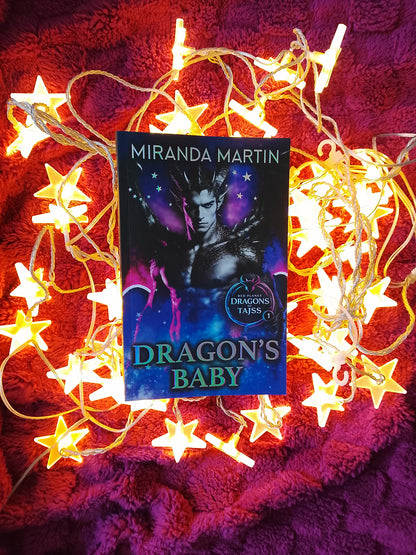 Book titled 'Dragon's Baby' by Miranda Martin surrounded by star-shaped lights on a textured red surface