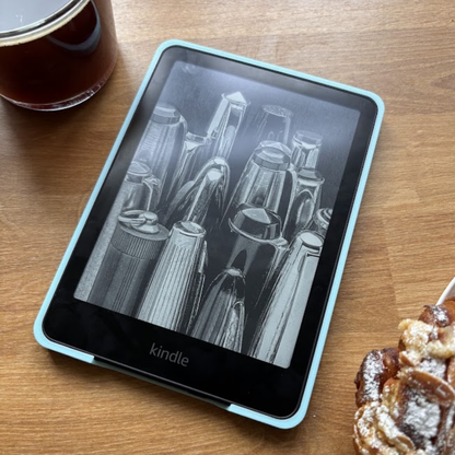 A Kindle e-reader displaying grayscale art of cocktail shakers, next to coffee and a pastry.